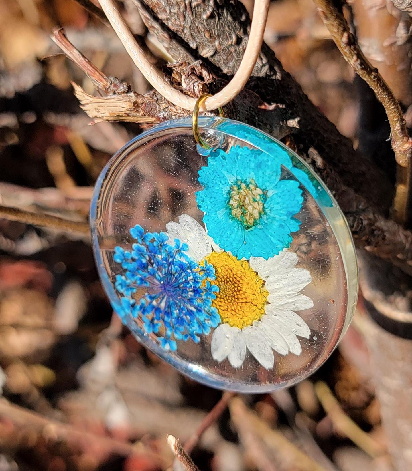 Exquisite handmade circular resin pendant containing white and blue flowers. A fantastic unique gift for a nature lover in your life.