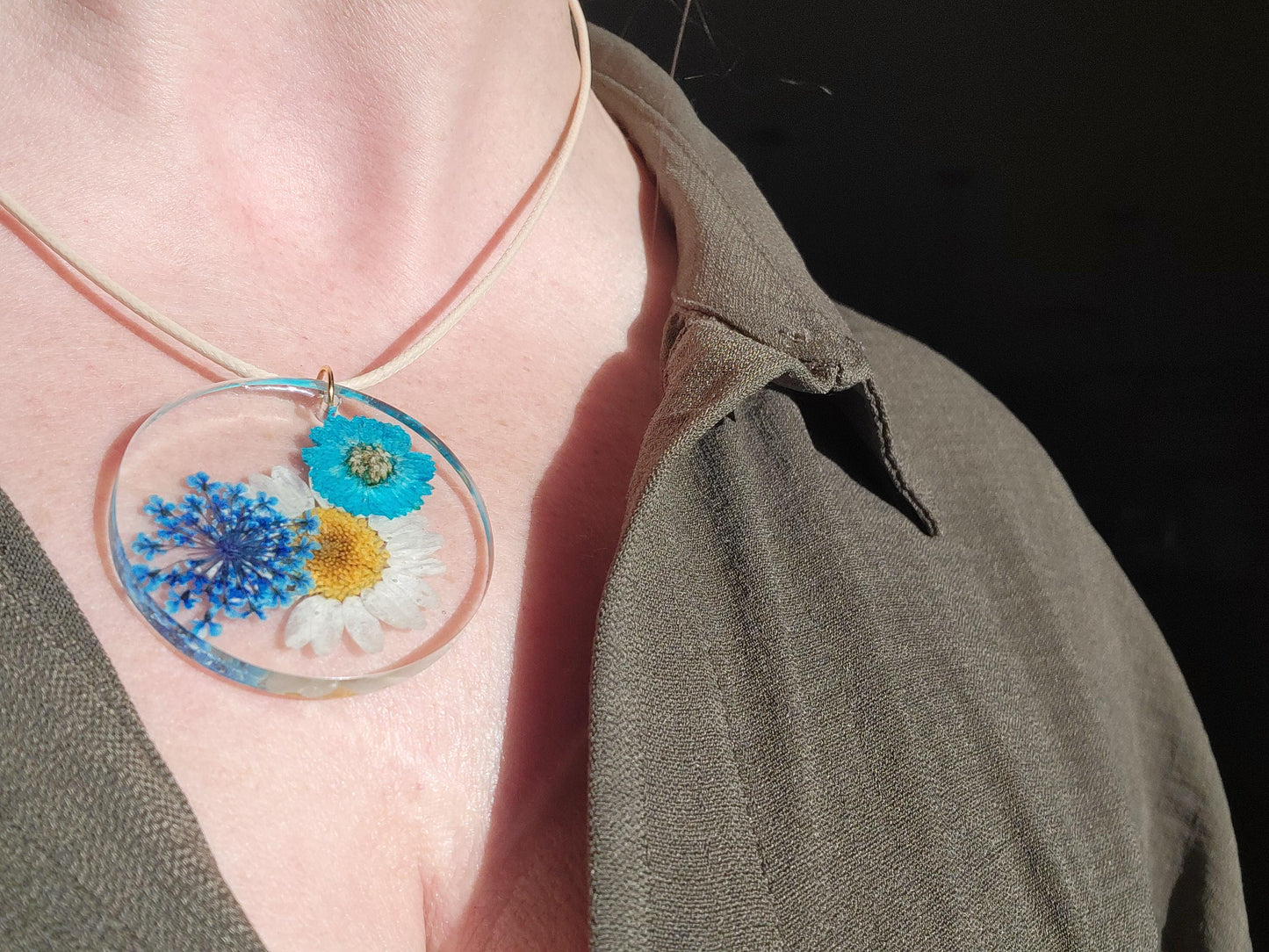 Exquisite handmade circular resin pendant containing white and blue flowers. A fantastic unique gift for a nature lover in your life.